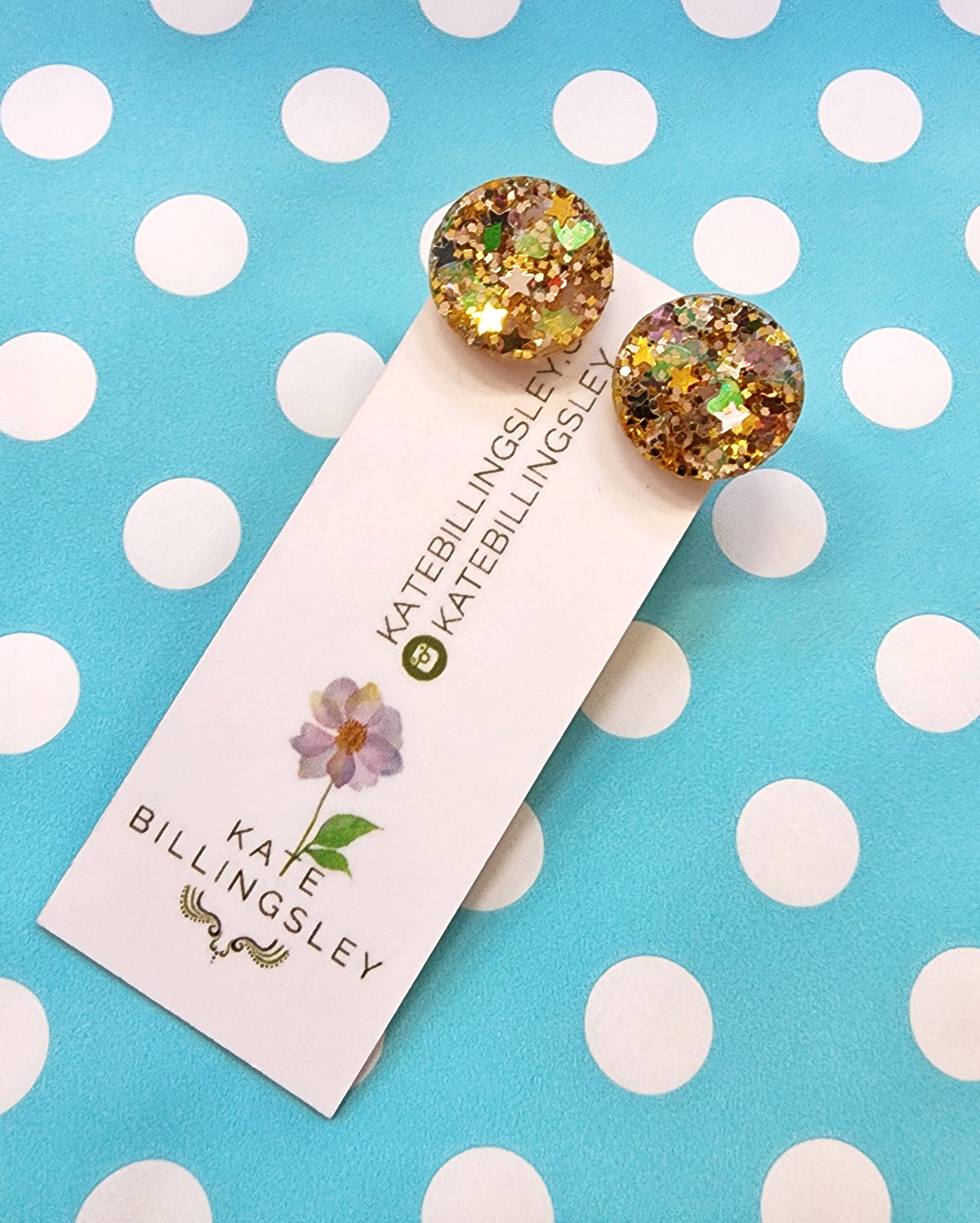 Glittery round earrings on a Kate Billingsley card against a polka dot background