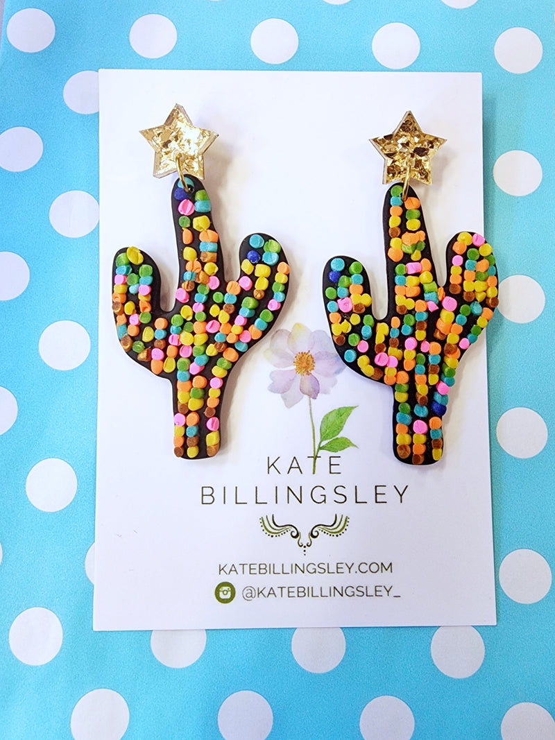Colorful cactus-shaped earrings on a Kate Billingsley card with a polka dot background